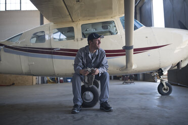 Mechaniker sitzt neben einem Leichtflugzeug in einem Flugzeughangar - ZEF12235