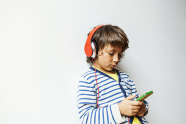 Little boy listening to the music of his smartphone with headphones - VABF00973