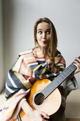 Junge Frau mit Decke und Gitarre, die lustige Gesichter zieht - VABF00987
