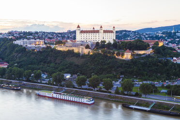 Slowakei, Bratislava, Blick auf die Burg mit einem Flusskreuzfahrtschiff auf der Donau im Vordergrund in der Dämmerung - WDF03837