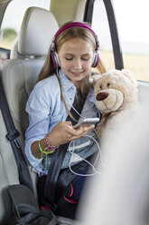 Mädchen sitzt im Auto, hält Teddybär und hört Musik - WESTF22341