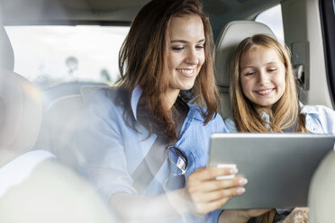 Mutter und Tochter auf Autoreise sitzen im Auto und schauen auf ein digitales Tablet - WESTF22345