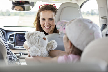 Mother and daughter on road trip sitting in car holding teddy bear - WESTF22353