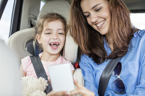 Mutter und Tochter auf Autoreise sitzen im Auto und schauen auf ihr Smartphone - WESTF22370