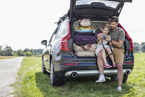 Vater und Tochter sitzen in einem offenen Kofferraum und schauen in die Kamera, als sie eine Pause von einer Autofahrt machen - WESTF22376