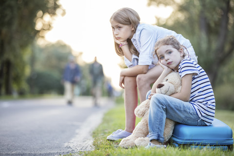 Two girls sitting on suitcase at the roadside stock photo