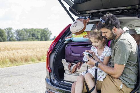 Vater und Tochter sitzen in einem offenen Kofferraum und schauen in die Kamera, als sie eine Pause von einer Autofahrt machen - WESTF22416