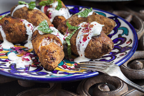 Kibbeh, orientalische Fleischkroketten mit Joghurtsoße auf einem Teller - SBDF03113