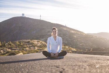 Young woman sitting cross-legged on empty road - SIPF01228