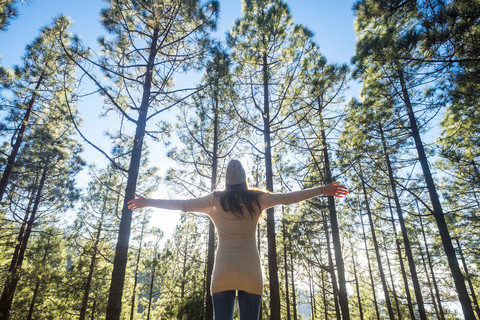 Rückenansicht einer Frau mit ausgestreckten Armen im Wald, lizenzfreies Stockfoto