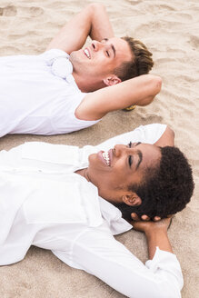 Glückliches junges Paar liegt nebeneinander am Strand mit den Händen hinter dem Kopf - SIPF01244
