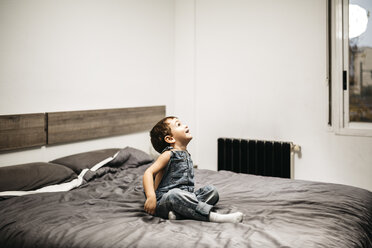 Kleiner Junge sitzt auf dem Bett seiner Eltern und schaut etwas - JRFF01114