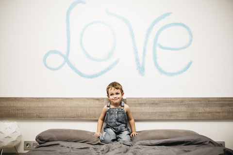 Kleiner Junge hockt auf dem Bett seiner Eltern, lizenzfreies Stockfoto