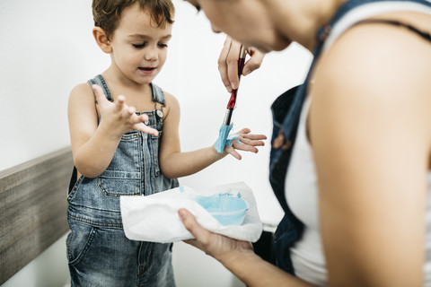 Mutter malt die Hände eines kleinen Jungen blau an, lizenzfreies Stockfoto