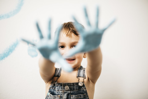 Porträt eines lächelnden kleinen Jungen, der seine Handflächen voller hellblauer Farbe zeigt, lizenzfreies Stockfoto