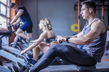 Young man exercising at rowing machine in gym - ZEF12267