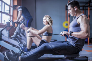 Young man exercising at rowing machine in gym - ZEF12268