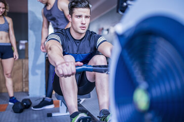 Young man exercising at rowing machine in gym - ZEF12273