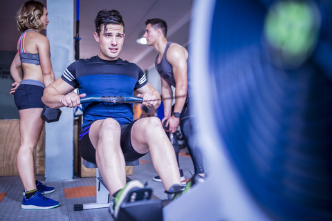 Junger Mann trainiert an einem Rudergerät im Fitnessstudio, lizenzfreies Stockfoto