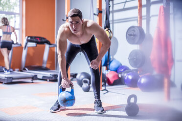 Young man lifting kettlebell in gym - ZEF12279