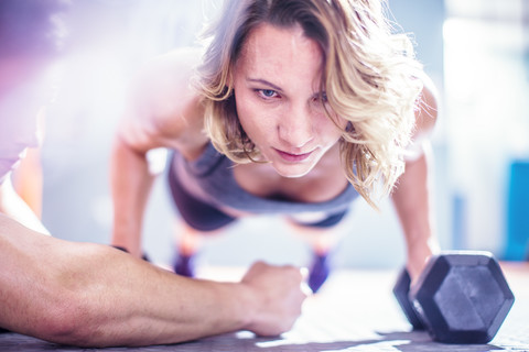 Fitness-Lehrer mit einer Frau, die im Fitnessstudio Hanteln hochdrückt, lizenzfreies Stockfoto
