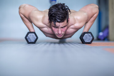 Young man doing dumbbell press ups in gym - ZEF12291