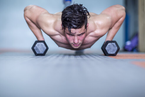 Junger Mann macht Liegestütze mit Hanteln im Fitnessstudio - ZEF12291