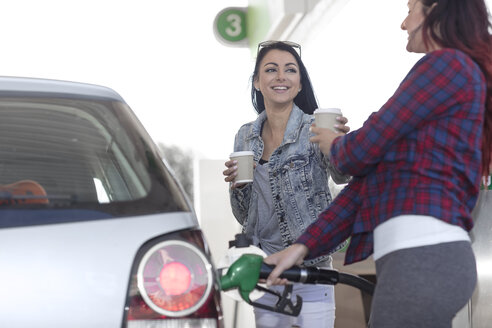 Zwei Frauen mit Kaffee zum Mitnehmen tanken Auto an einer Tankstelle - ZEF12296