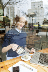 Lächelnde junge Frau mit Laptop und Tasse Tee in einem Cafe - VABF01003