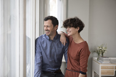 Laughing couple looking through window at home - RBF05422