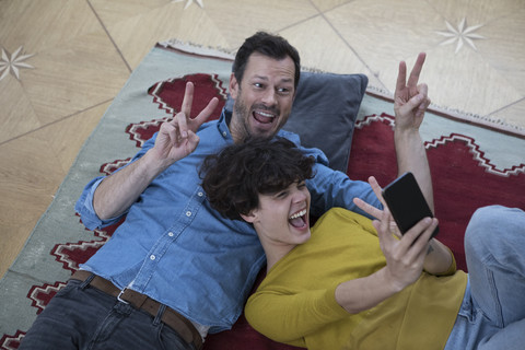 Paar liegt zusammen auf dem Teppich und macht ein Selfie mit Smartphone, lizenzfreies Stockfoto