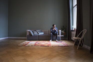 Man sitting on couch at home looking through window - RBF05441