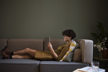 Lächelnde junge Frau mit Tablet auf der Couch zu Hause - RBF05446