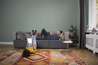 Ein Paar, das sich im Wohnzimmer mit verschiedenen elektronischen Geräten entspannt - RBF05448
