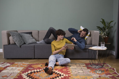 Paar entspannt zusammen im Wohnzimmer und schaut auf ein Tablet - RBF05449