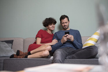 Paar sitzt zusammen auf der Couch und schaut auf sein Handy - RBF05450