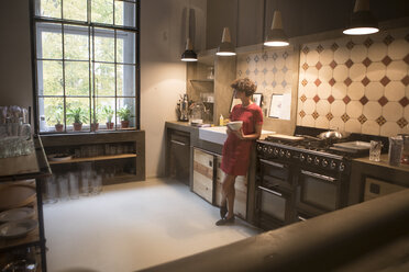 Young woman standing in the kitchen looking through window - RBF05469