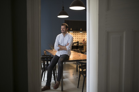 Lächelnder Mann sitzt am Tisch in seiner Küche, lizenzfreies Stockfoto