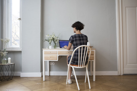 Rückenansicht einer jungen Frau, die zu Hause am Schreibtisch sitzt und einen Laptop benutzt, lizenzfreies Stockfoto