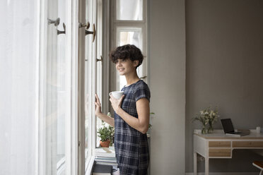 Portrait of smiling young woman looking through window at home - RBF05505