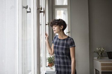 Portrait of young woman looking through window at home - RBF05506