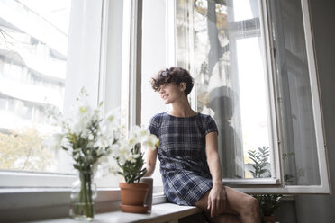 Junge Frau sitzt zu Hause auf der Fensterbank - RBF05507