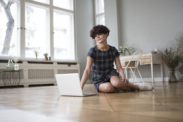 Young woman sitting on the floor at home looking at laptop - RBF05510