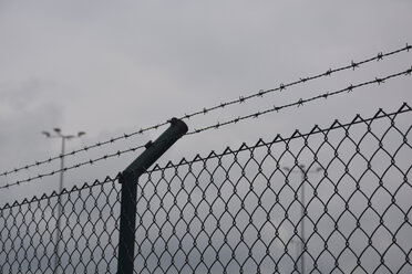 Barbed wire fence and wire mesh fence in front of grey sky - AXF00793