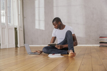 Young man sitting on floor with laptop and tablet - FMKF03394