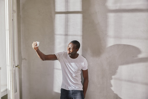 Lächelnder junger Mann nimmt Selfie mit Handy, lizenzfreies Stockfoto