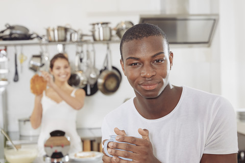 Porträt eines lächelnden jungen Mannes mit Kaffeetasse in der Küche, lizenzfreies Stockfoto