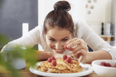 Portrait of happy young woman garnishing waffles in the kitchen - FMKF03412