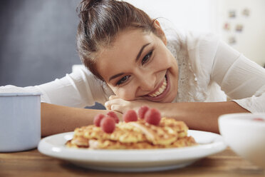 Portrait of happy young woman looking at waffles in the kitchen - FMKF03413