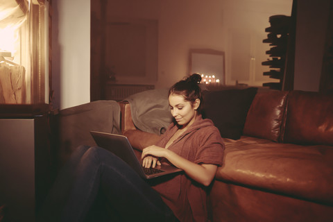 Junge Frau entspannt mit Laptop im beleuchteten Wohnzimmer, lizenzfreies Stockfoto